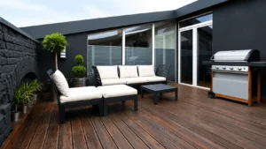 Modern outdoor patio with wood decking, lounge furniture, large windows, potted plants, and barbecue grill.