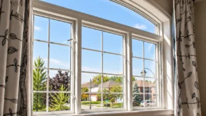 Large arched residential window with white frames overlooking a sunny suburban neighborhood.
