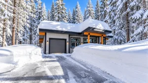 Modern home surrounded by snow-covered evergreen trees with deep snowbanks along the driveway.