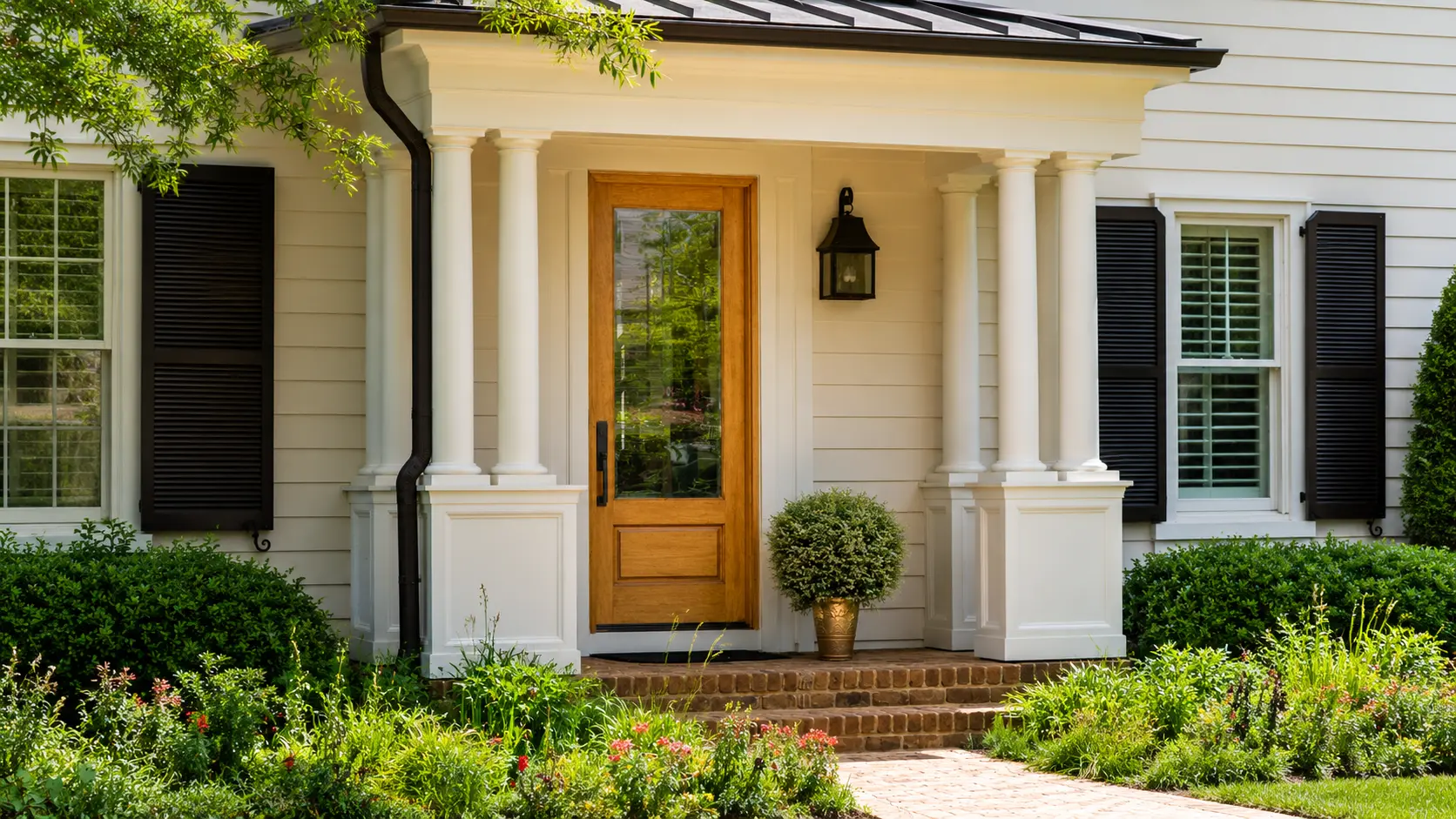 Traditional home entrance with wood front door, white columns, black shutters, and landscaped garden.